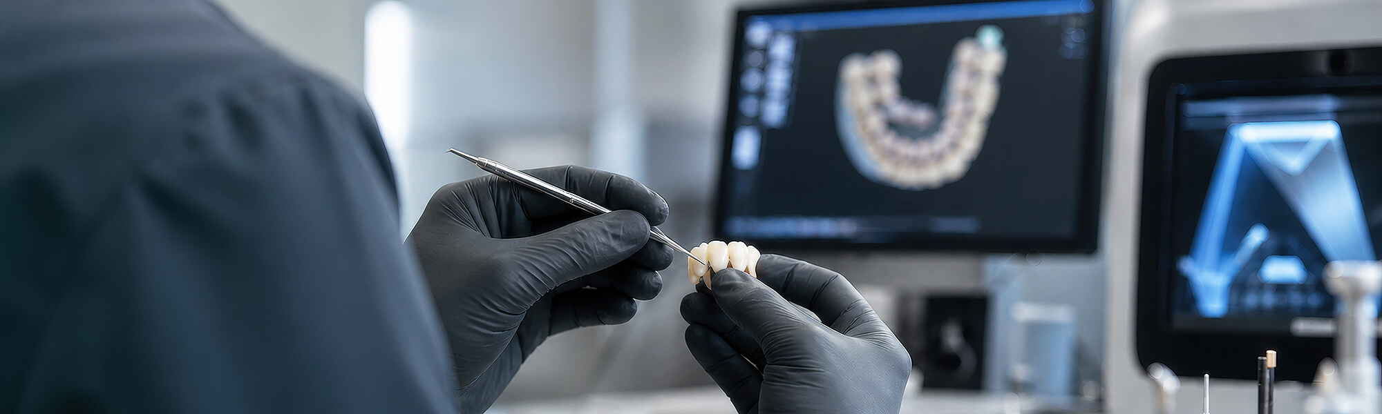 Zahntechniker bearbeitet eine Zahnrestauration vor digitalen CAD/CAM-Bildschirmen